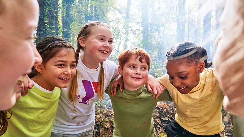 smiling kids make a team hudle in the woods during summer camp