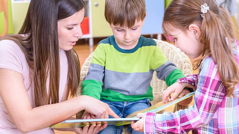 Teacher helps two young children with their reading skills