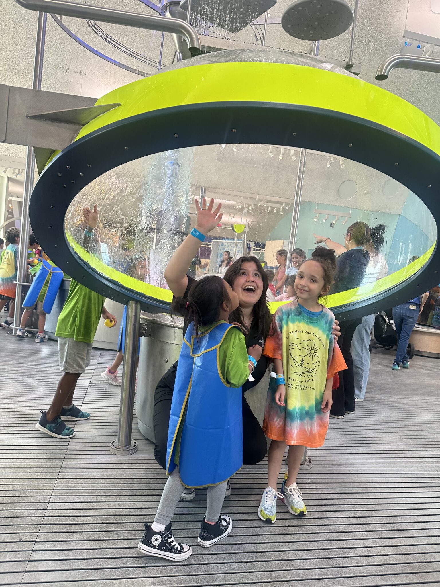 Staff member and two young children at an interactive water exhibit during Armed Services YMCA El Paso Operation Summer Camp field trip.