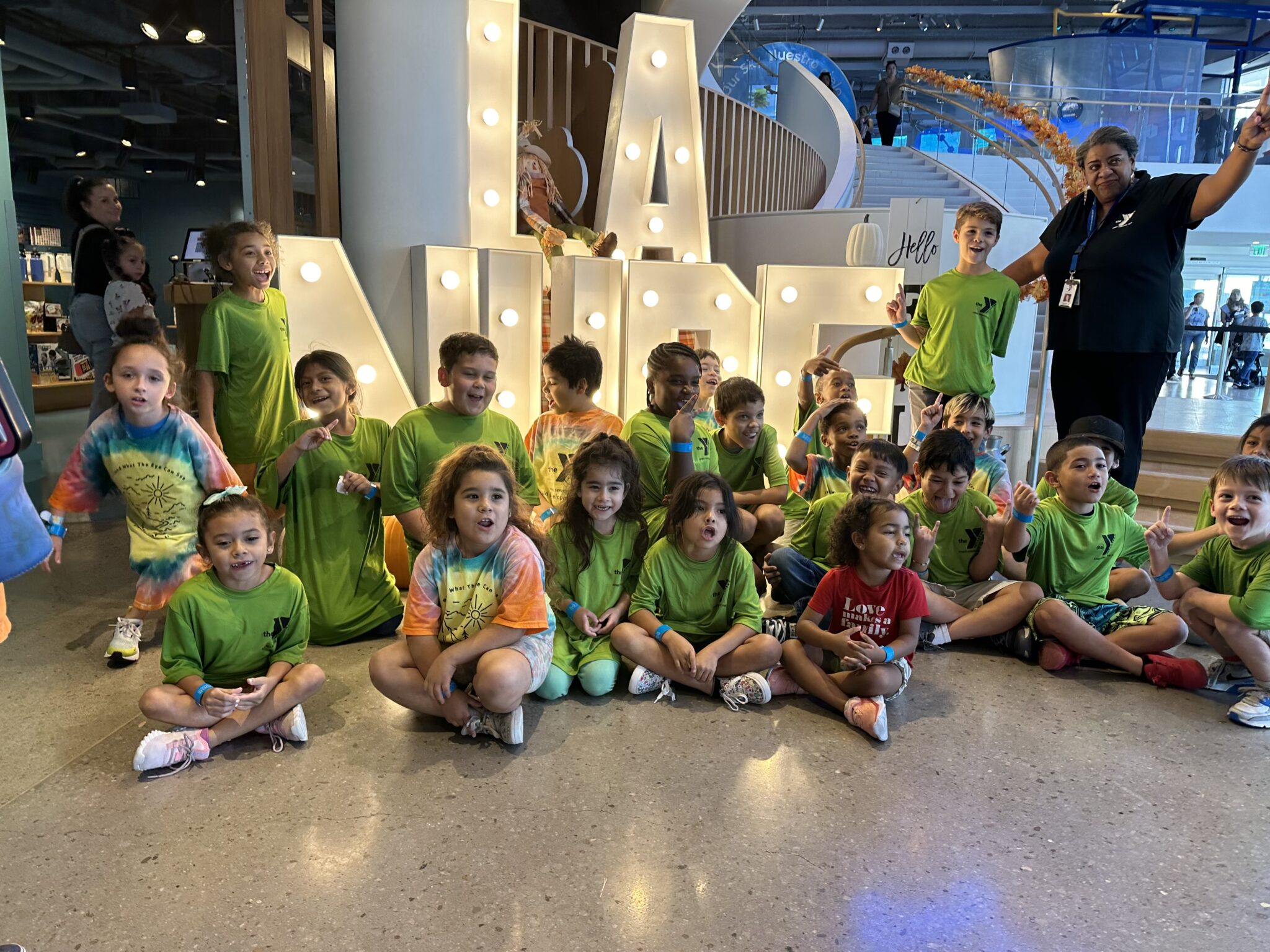 Group of children and staff from Armed Services YMCA El Paso Summer Camp posing in front of the illuminated “LA NUBE” sign during a field trip.